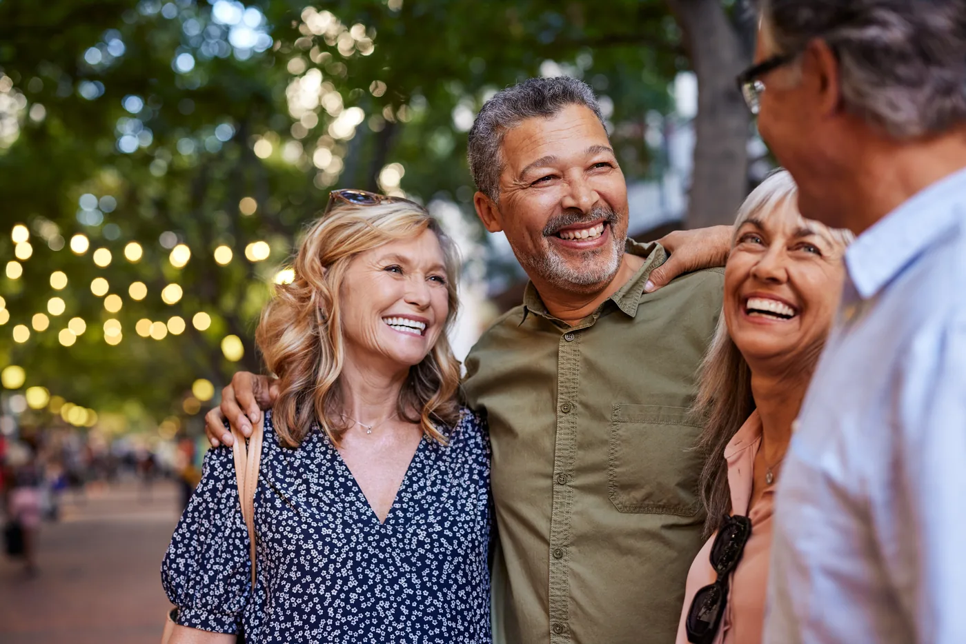 Four friends of retirement age laughing together on a tree-lined street at dusk